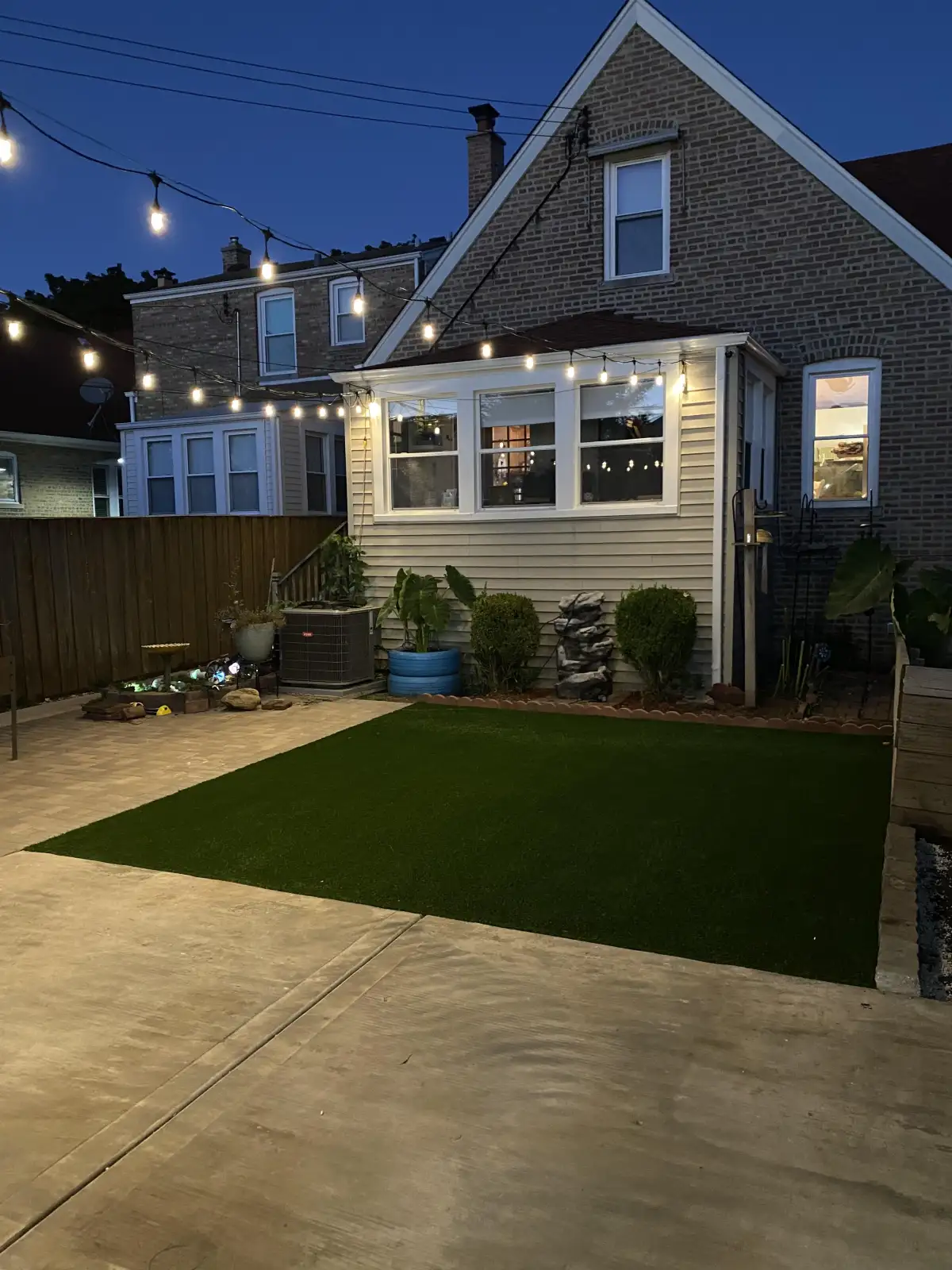 Backyard turf and patio under overhead string lights in the evening