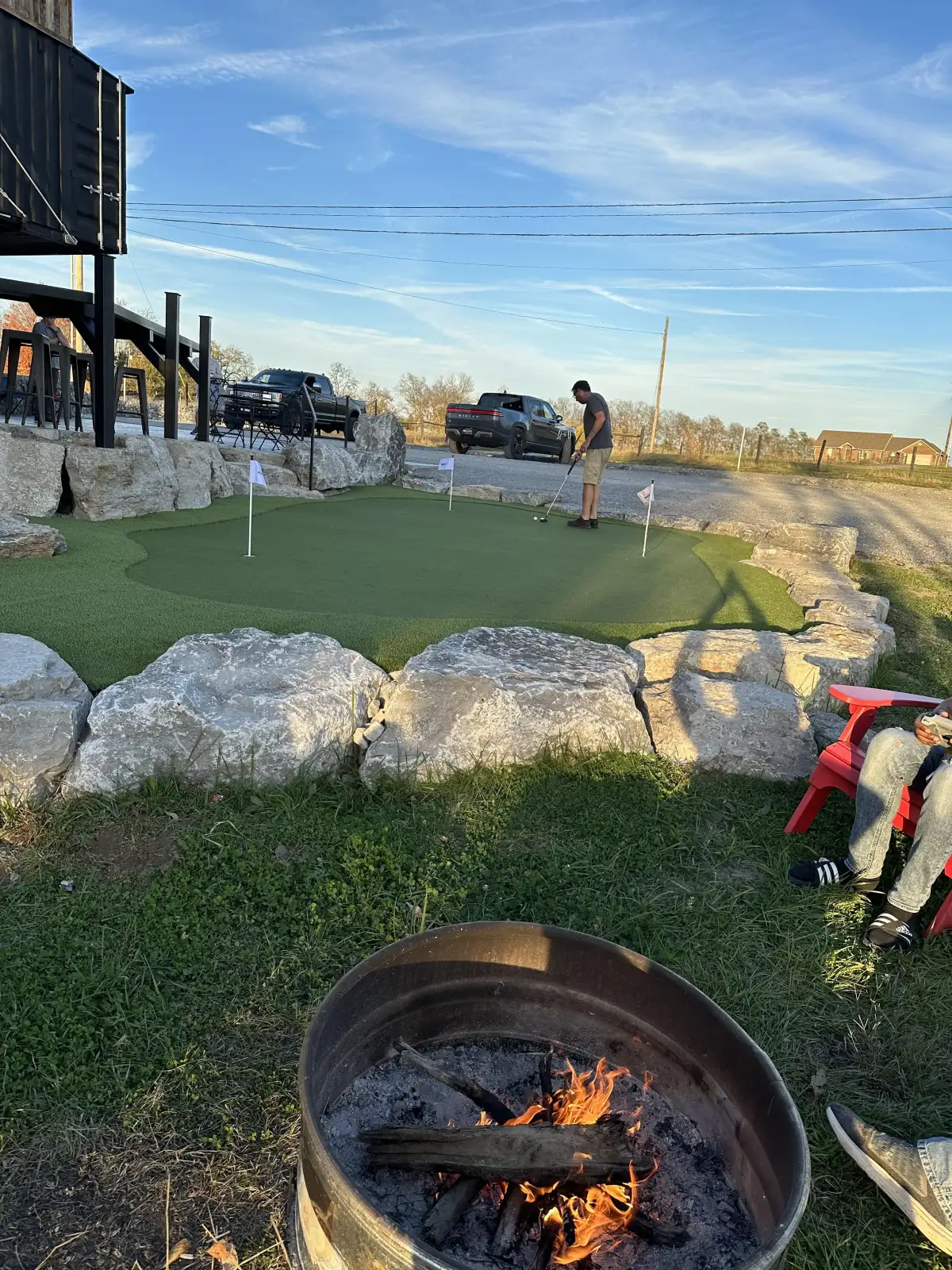 Custom putting green with natural boulder edging and fire pit in backyard setting