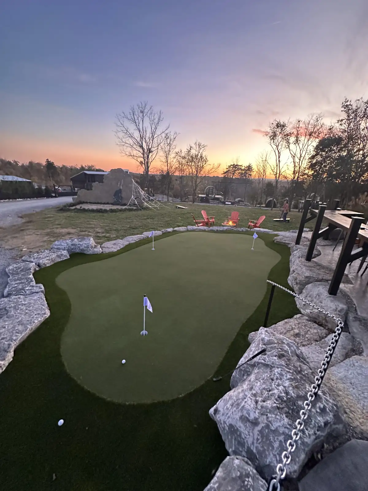 Wide panoramic view of a backyard putting green at sunset with purple and orange sky