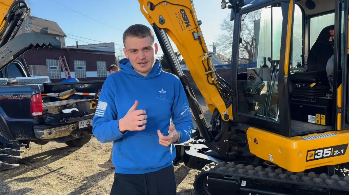 Great Lakes Synthetic Turf team member in branded hoodie with excavator on site